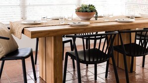 Un comedor con una mesa de madera, sillas negras, una lámpara colgante tejida y una planta grande en maceta.