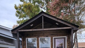 Una cabaña de madera pequeña con un porche, dos ventanas grandes y una puerta.
