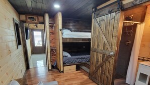 Un interior de cabaña acogedor con una litera, un sofá, pisos de madera y una puerta rústica.