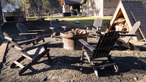 Un área de estar al aire libre de estilo rústico con sillas Adirondack, una chimenea y una estructura de madera con techo inclinado.