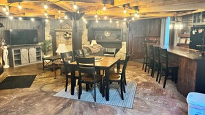 A rustic interior with a wooden dining table, chairs, a sofa, and a bar area.