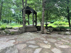 A wooden gazebo with a stone base, surrounded by a stone pathway and large rocks.