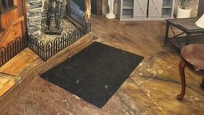 A rustic interior with a stone wall, wooden beams, a mounted TV, and a black rug.