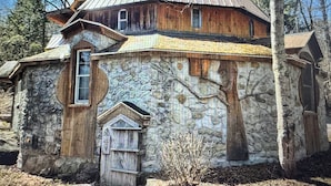 A rustic stone building with a sloped metal roof, a wooden door, and a small window.