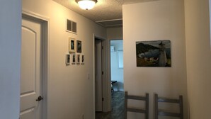Un corridoio con una porta bianca, una luce a soffitto e un quadro raffigurante un faro.