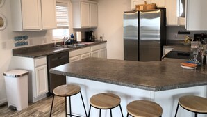 Una cucina moderna con mobili bianchi, un frigorifero in acciaio inossidabile, un piano di lavoro in granito e sgabelli da bar in legno.