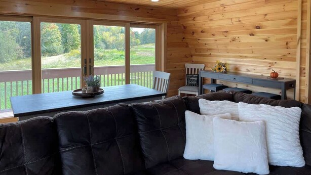 Ein Holzblockhaus-Innenraum mit großem Fenster, Esstisch, einer Couch und einer Bank.
