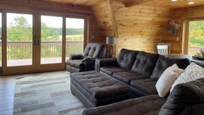 Ein Holzinnenraum mit einem Ecksofa, einer Lampe und Blick durch große Schiebetüren.