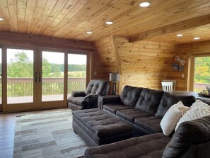 Un interior de madera con un sofá seccional, una lámpara y vistas a través de grandes puertas correderas.