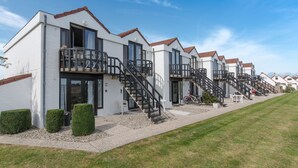 A row of modern, white buildings with brown roofs and black railings, featuring balconies and a gravel pathway. - Marlene with parking and shared pool by Interhome (De Haan)