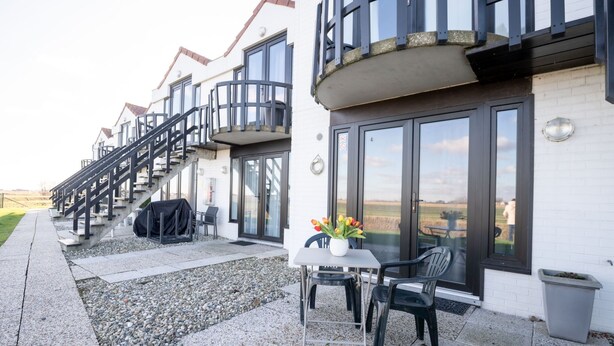 A modern building with a balcony, outdoor seating area, and a staircase leading to the upper floors. - Marlene with parking and shared pool by Interhome (De Haan)