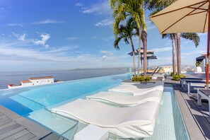 An infinity pool with lounge chairs and umbrellas, overlooking a body of water. - DTerrace Penthouse1 Best Ocean Views Romantic Zone (Puerto Vallarta)