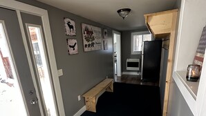 A hallway with a wooden bench, a black rug, and a refrigerator.