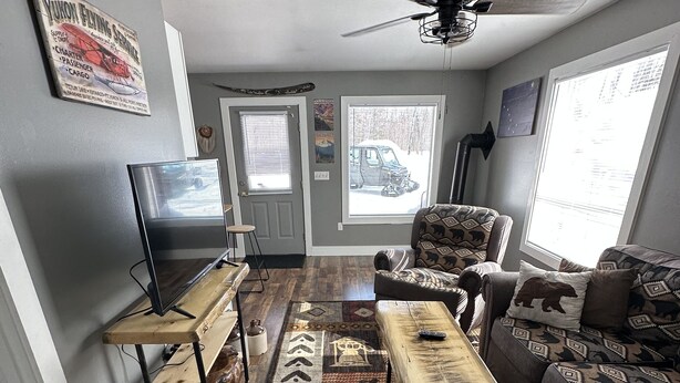 A living room with a large window, a ceiling fan, a TV, a sofa, a coffee table, and a rug.