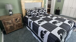 A bedroom with a large bed, a wooden nightstand, a lamp, a quilted bedspread, and a door leading to another room.