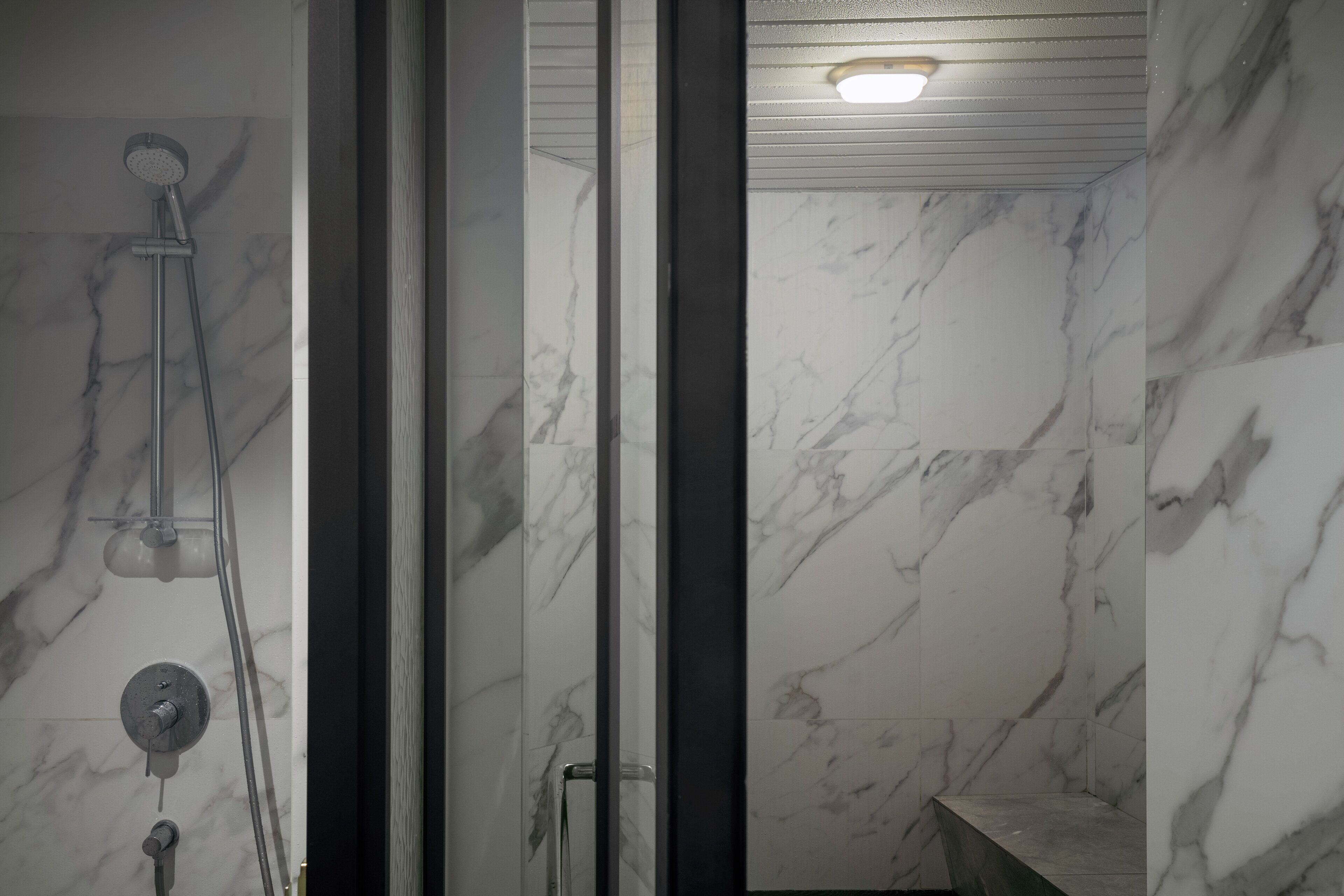 Une salle de bain moderne avec des murs en marbre, une cabine de douche en verre et un pommeau de douche apparent.