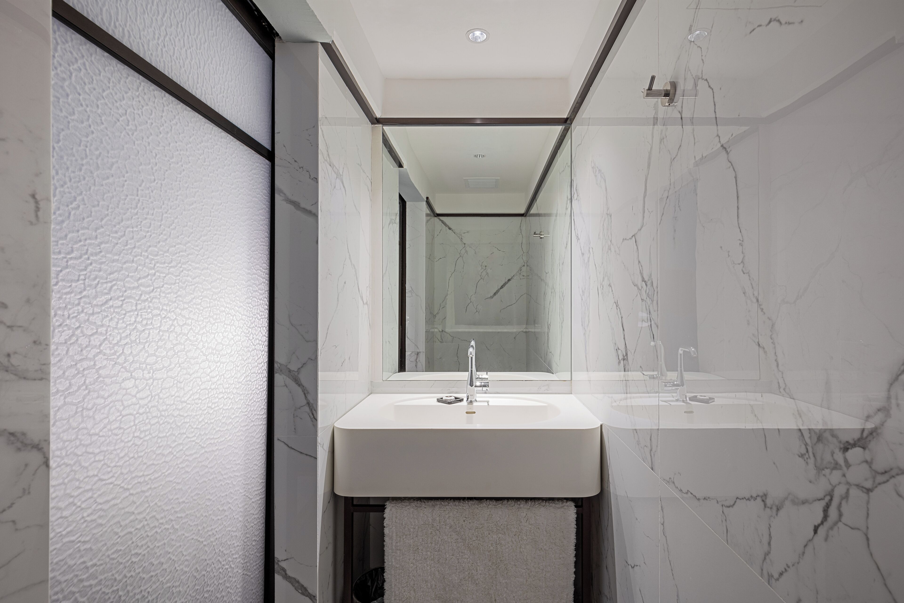 A modern bathroom with a marble sink, a mirror, and a shower.
