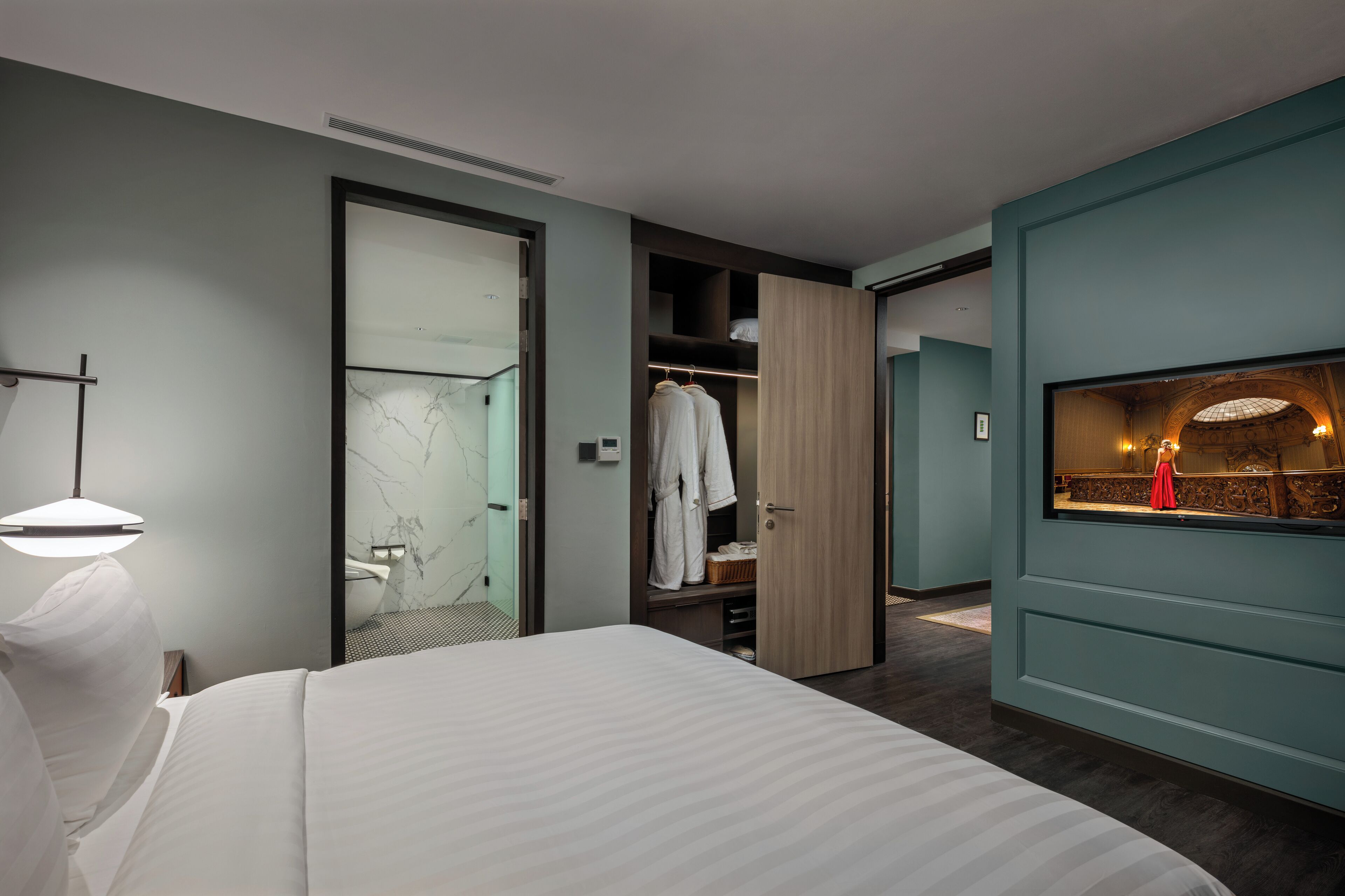 A modern hotel room with a large bed, a walk-in closet, and a bathroom with a glass shower.