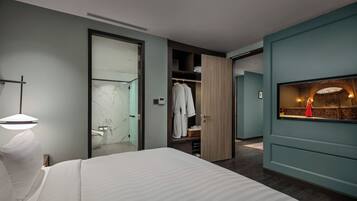 A modern hotel room with a large bed, a walk-in closet, and a bathroom with a glass shower.