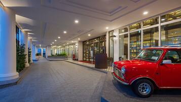 Um corredor de hotel moderno com um carro vintage vermelho estacionado à direita.