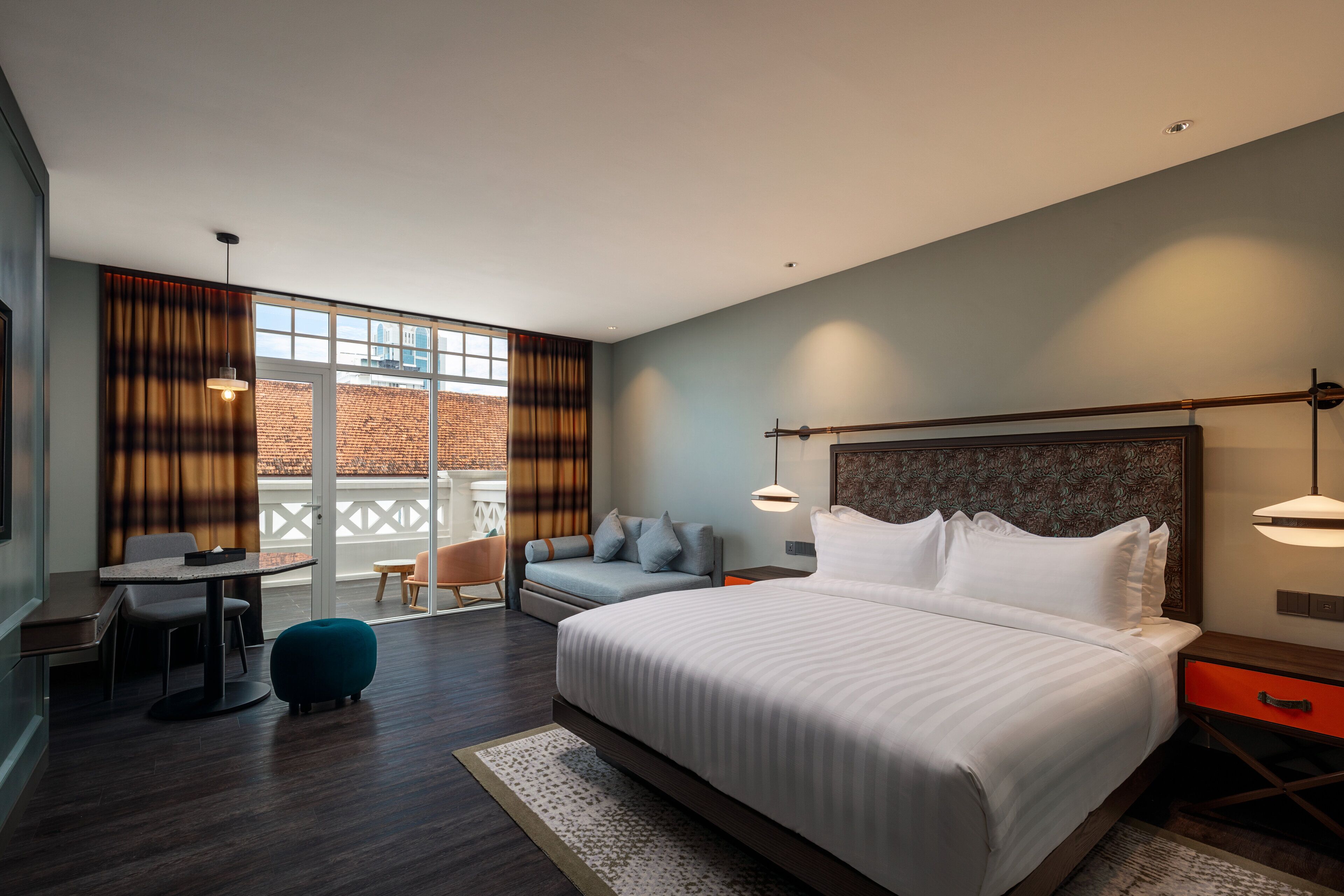 A modern hotel room with a large bed, a seating area with a sofa and chairs, a small table, and a balcony with a view of a brick building.