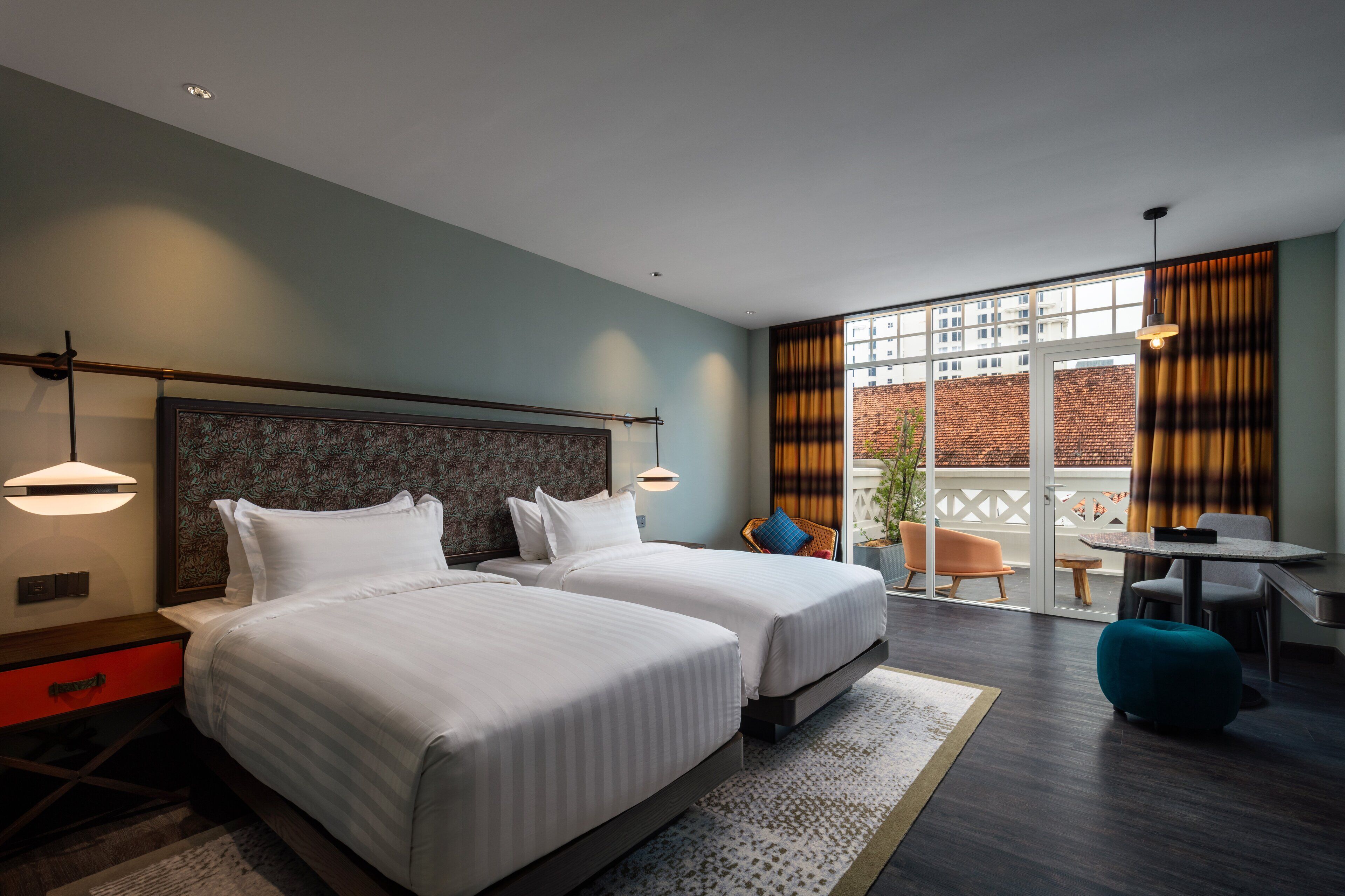 A hotel room with two beds, a dining area, and a balcony with a view of buildings.