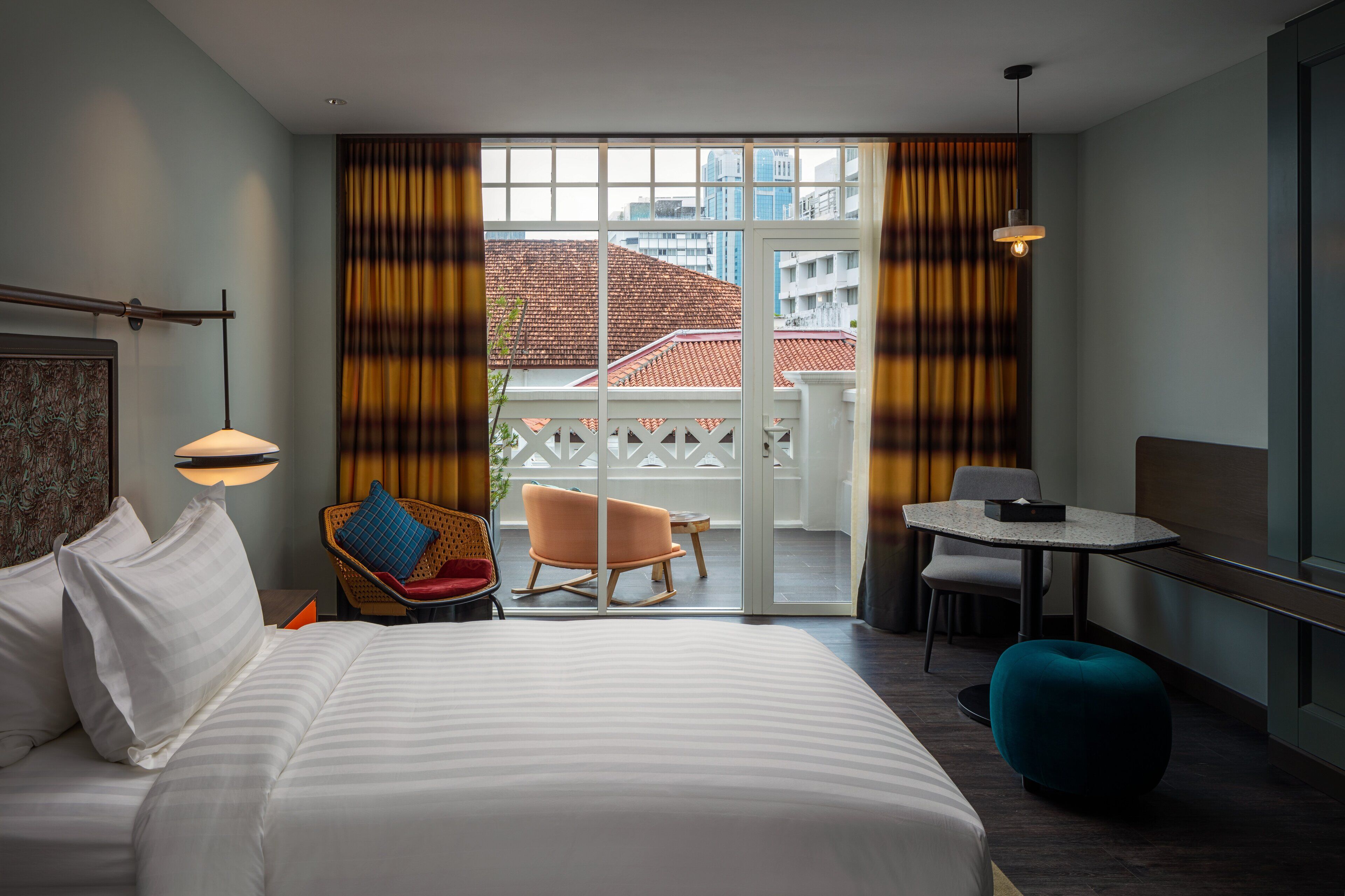 Habitación de hotel con una cama grande, un rincón de estar con una mesa y sillas, un balcón con cortinas y vistas a la ciudad.