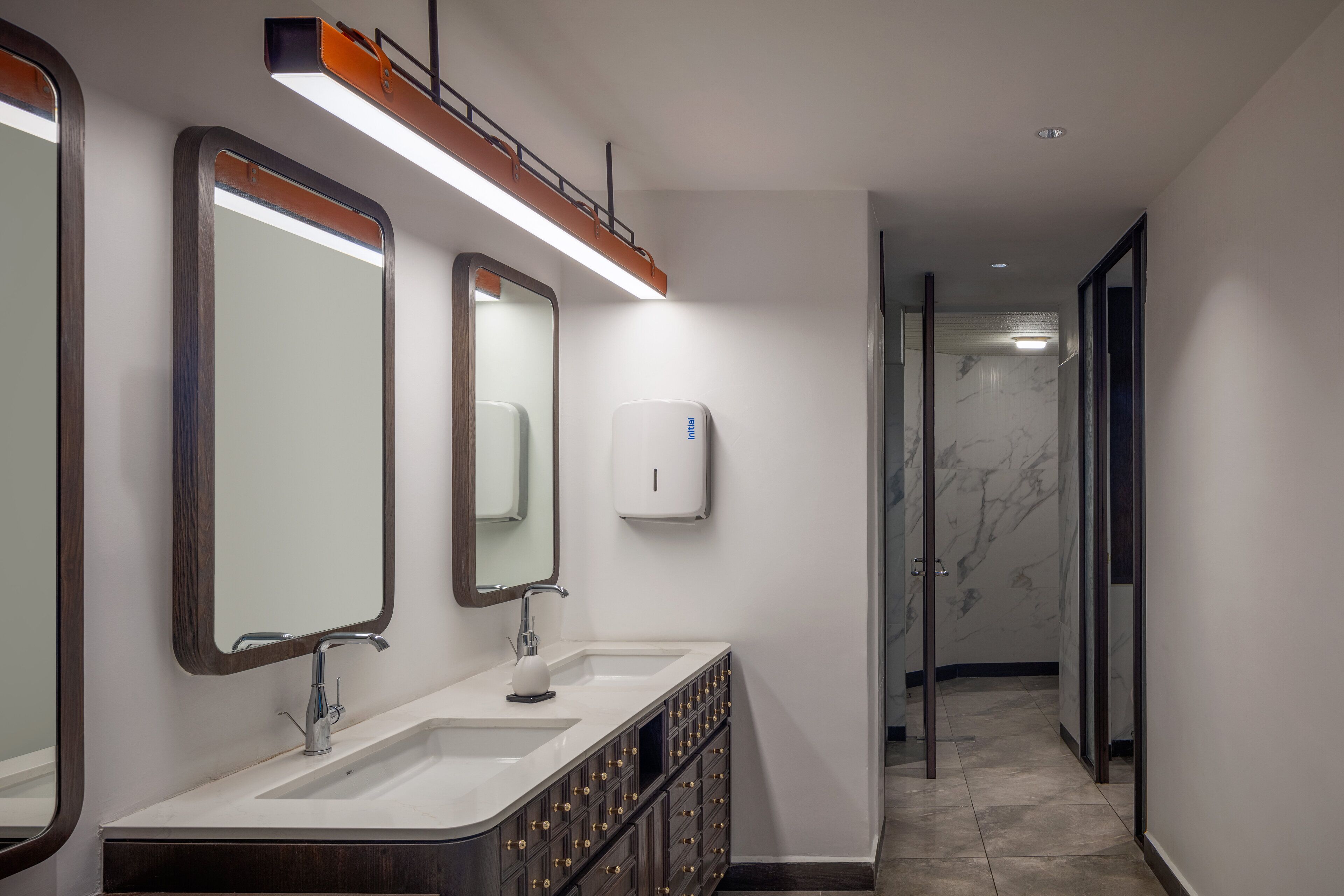 A modern bathroom with two sinks, a mirror, and a hand sanitizer dispenser.