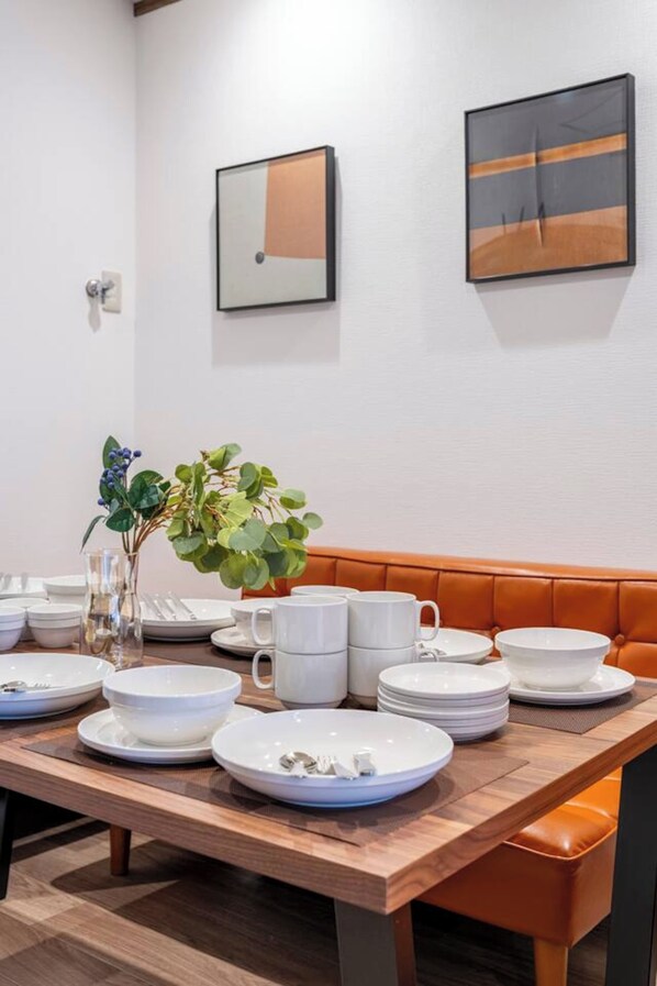 Un coin repas avec une table en bois dressée pour quatre personnes, un banc et deux œuvres d’art encadrées accrochées au mur.