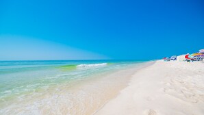 A beach with clear turquoise water, white sand, and colorful umbrellas. - Crystal Tower 1102 2 Bedroom Condo (Gulf Shores)
