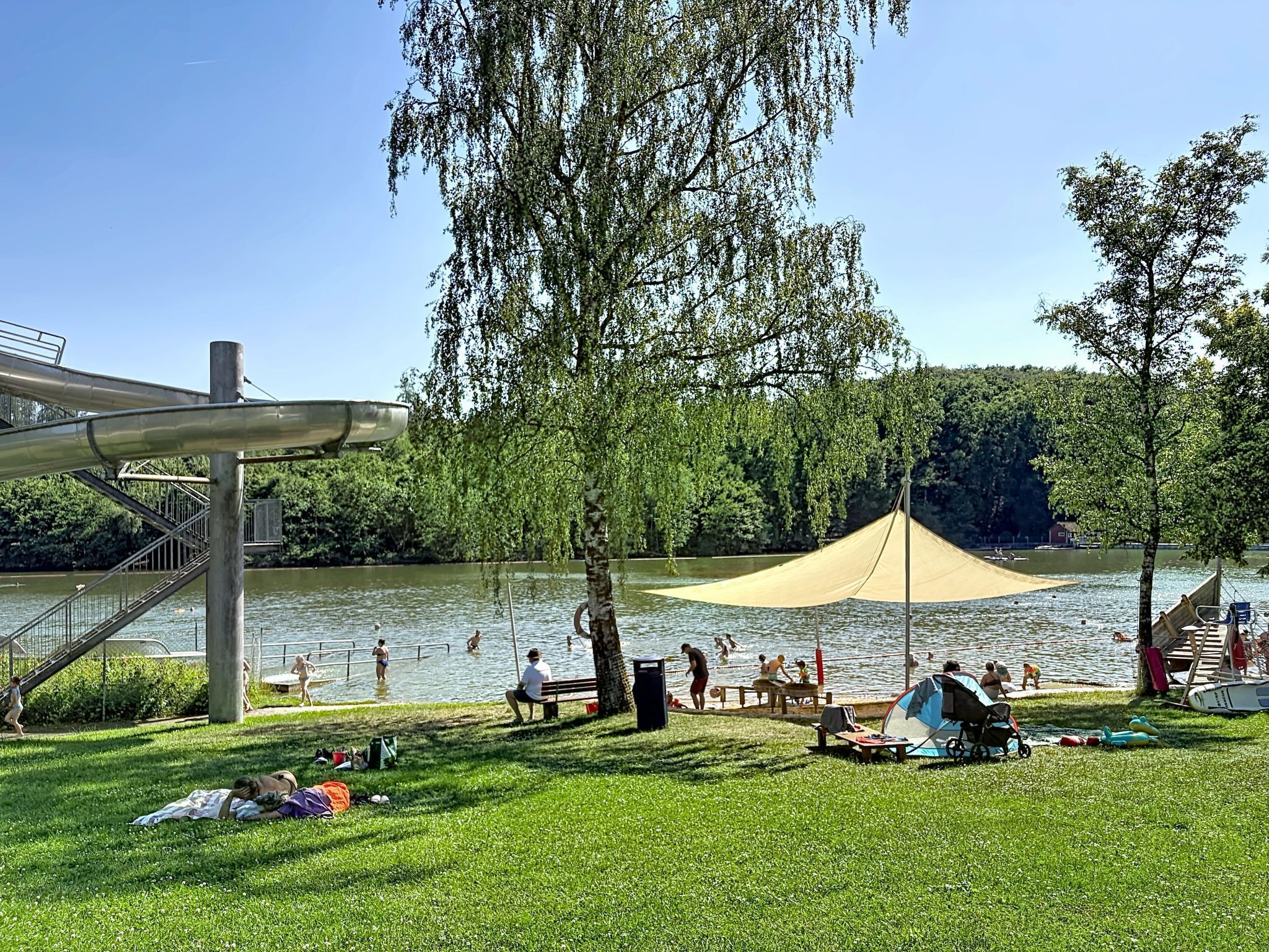 Een park aan het meer met een picknickplaats, een speeltuin en een zwemgedeelte.
