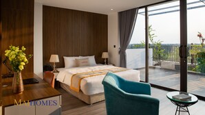 A modern hotel room with a large bed, a desk with a laptop, a vase of flowers, and a balcony with a view. - Maihomes hotel & Serviced Apartment (Vinh Phuc)