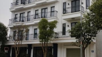 Un hôtel à plusieurs étages, doté de balcons, avec une voiture rouge garée devant.