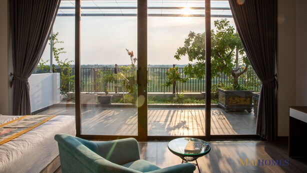 A bedroom with a large sliding glass door leading to an outdoor balcony with a view of the city. - Maihomes hotel & Serviced Apartment (Vinh Phuc)