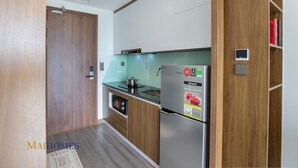 A compact kitchen with wooden cabinets, a stainless steel refrigerator, and a built-in oven. - Maihomes hotel & Serviced Apartment (Vinh Phuc)