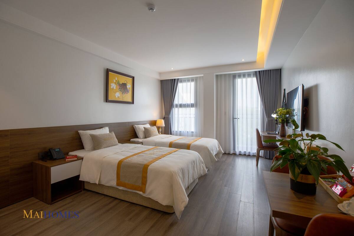A hotel room with two beds, a desk, a chair, a TV, and a potted plant.