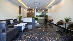 A modern lobby with black marble flooring, leather sofas, a reception desk, and potted plants. - Maihomes hotel & Serviced Apartment (Vinh Phuc)