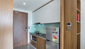 A compact kitchen with wooden cabinets, a stainless steel refrigerator, and a built-in oven. - Maihomes hotel & Serviced Apartment (Vinh Phuc)