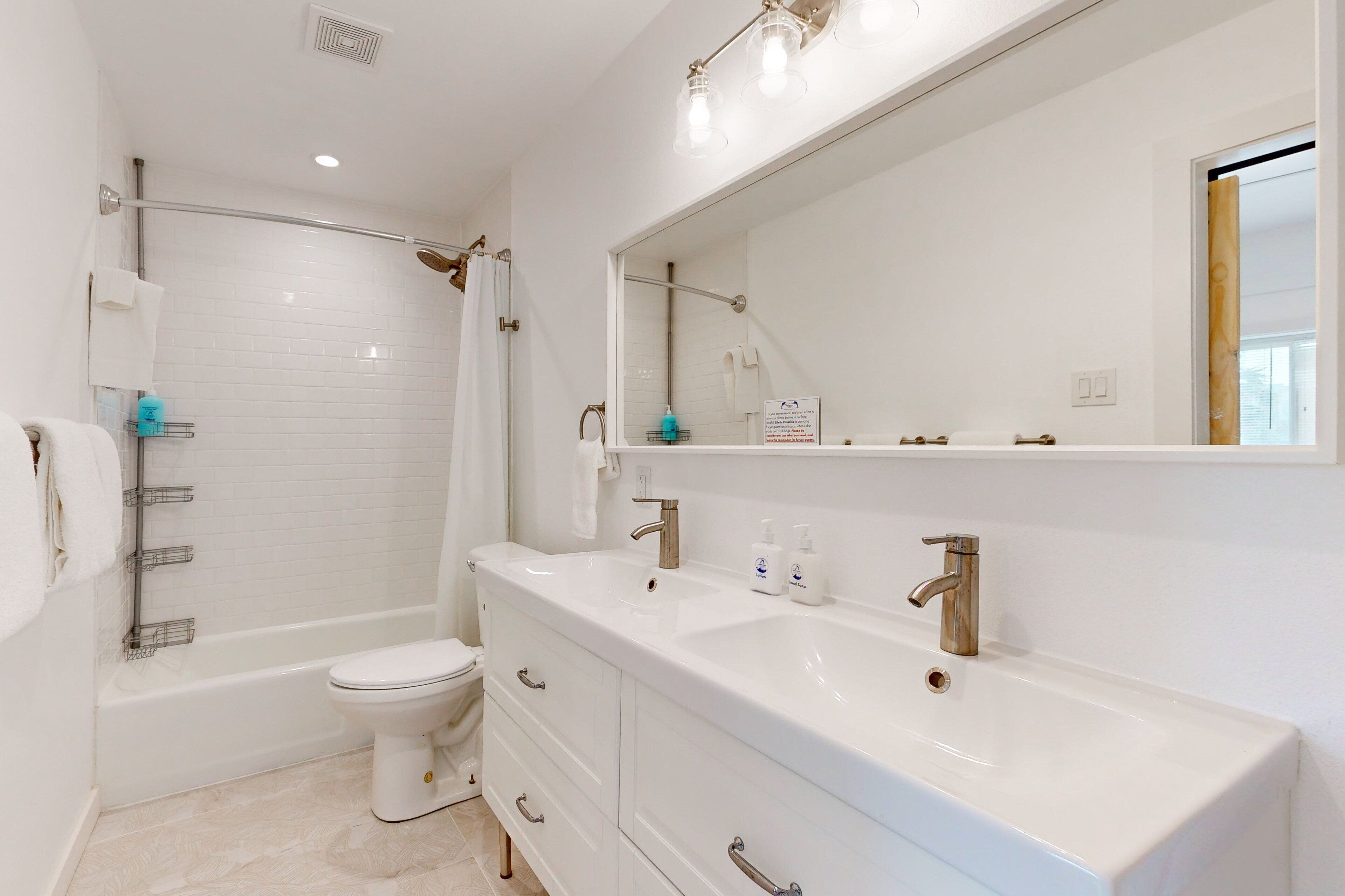 Un baño moderno con bañera, inodoro y un mueble de tocador grande con espejo.
