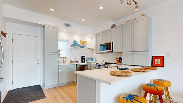 A modern kitchen with white cabinetry, a central island with stools, and a microwave above the island. - Walk to Sandfest , Shared Pool, Board Walk to Beach (Port Aransas)