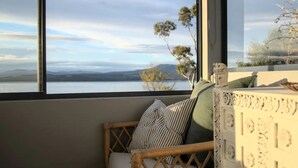 A room with a view of a lake and mountains, a wicker chair with cushions, and a decorative wall panel.