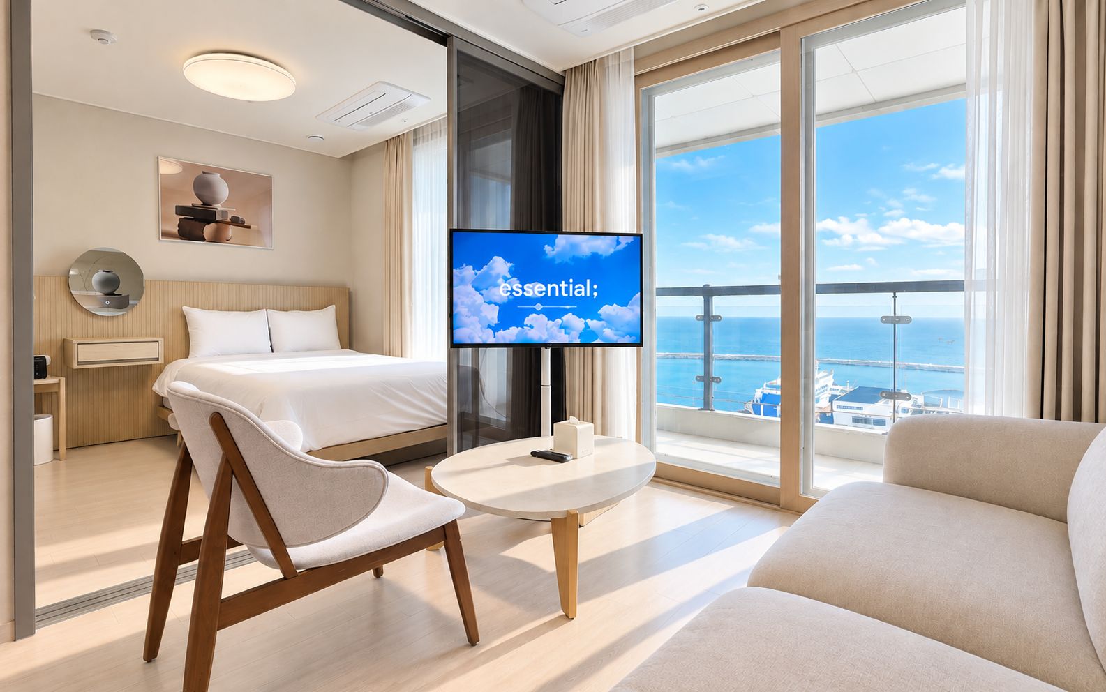 Moderni hotellihuone, jossa on sänky, televisio, merinäköalalla varustettu parveke ja oleskelualue.