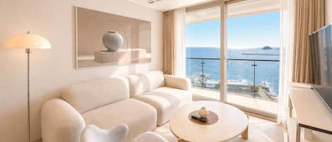 Une chambre d’hôtel moderne équipée d’un canapé, d’un fauteuil, d’une table ronde et d’un téléviseur.