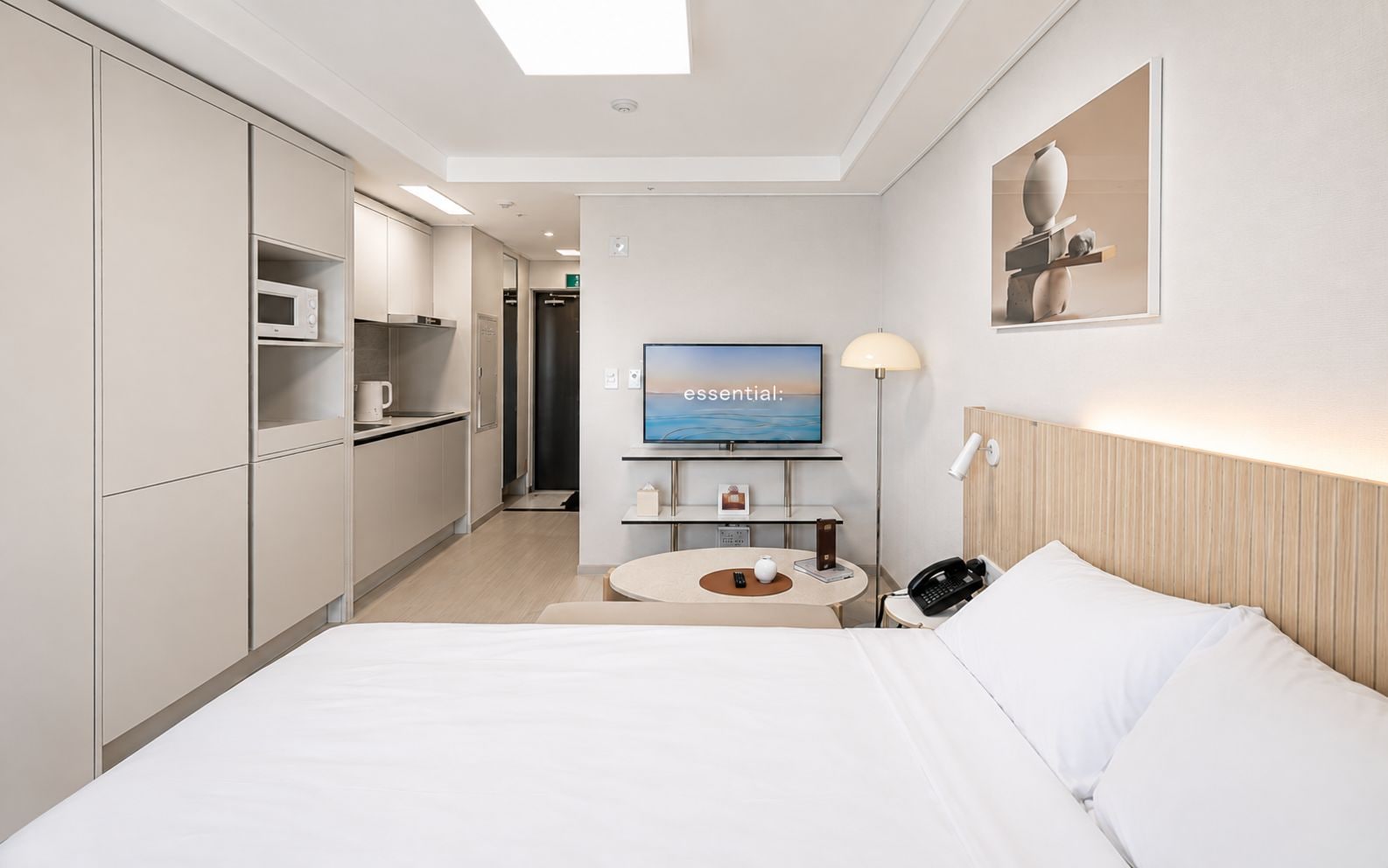 A hotel room with a bed, bedside table, lamp, and a television on the wall.