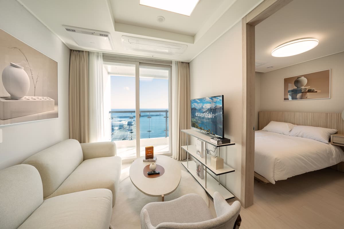 A modern hotel room with a large bed, a sofa, a coffee table, and a TV on a stand.