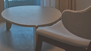 A room with a round table and a cushioned chair, a large window with a view of the sea, and a mounted television on the wall. - UH FLAT THE SOKCHO (Sokcho)