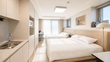 Ein Hotelzimmer mit Küchenzeile, zwei Betten, einem Nachttisch, einer Lampe und einem Fenster mit Vorhängen.