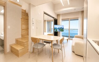 Habitación de hotel moderna con comedor, sofá, televisor y vista al mar.