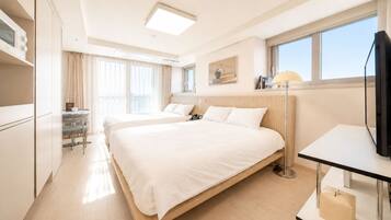 Ein Hotelzimmer mit einem großen Bett, Nachttischen, einem Schreibtisch, einem Sessel, einem Fernseher und einem Fenster mit Vorhängen.