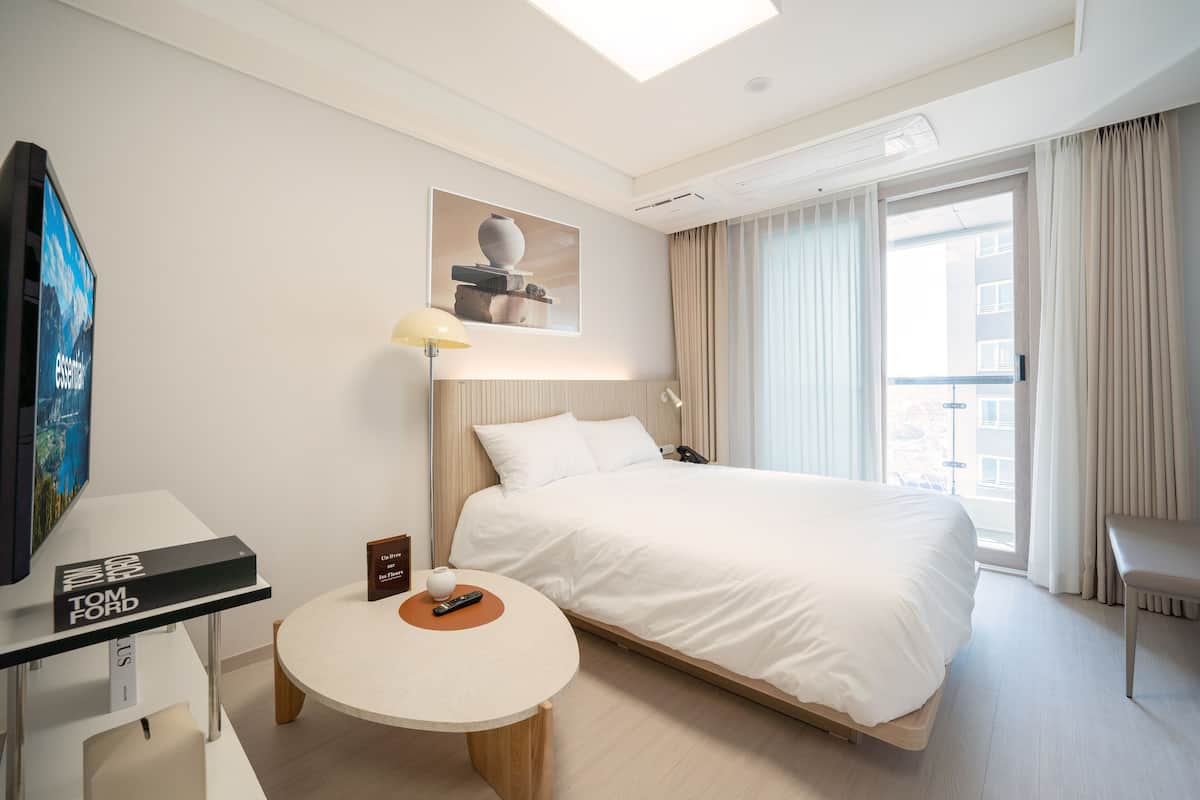 A modern hotel room with a large bed, a desk with a computer, a small table, and a TV.